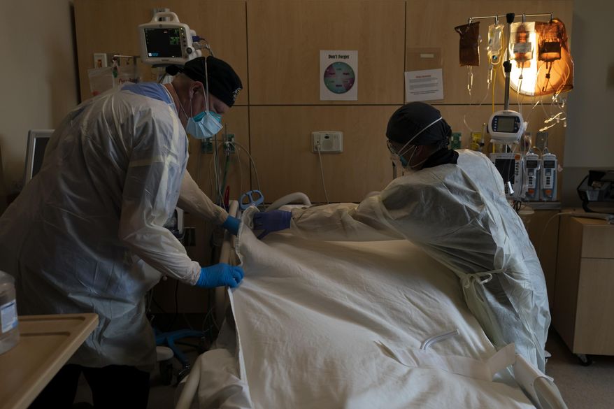 Respiratory therapist Frans Oudenaar, left, and registered nurse Bryan Hofilena cover a body of a COVID-19 patient with a sheet at Providence Holy Cross Medical Center in Los Angeles, Dec. 14, 2021. The fast-moving omicron variant may cause less severe disease on average, but COVID-19 deaths in the U.S. are climbing and modelers forecast 50,000 to 300,000 more Americans could die by the time the wave subsides in mid-March. (AP Photo/Jae C. Hong, File)
