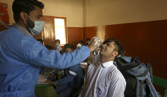 A heath worker takes a nasal swab sample from a student to test for the coronavirus at a school, in Karachi, Pakistan, Wednesday, Jan. 19, 2022. (AP Photo/Fareed Khan)