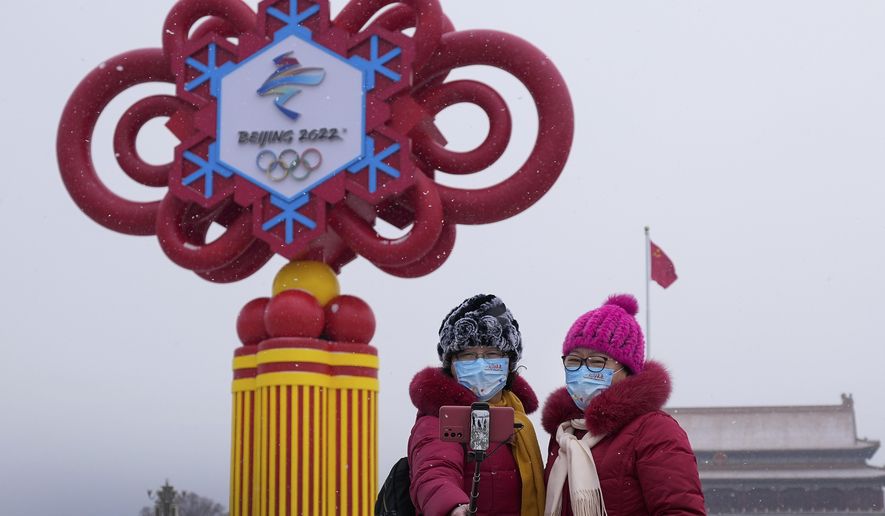 Women wearing face masks printed with a slogan for Beijing Winter Olympics Games take a selfie with a decoration for the Winter Olympics Games on Tiananmen Square in Beijing, Thursday, Jan. 20, 2022. With just over two weeks before the opening of the Beijing Winter Olympics, residents of the Chinese capital say they&#39;re disappointed at not being able to attend events because of coronavirus restrictions that have seen parts of the city placed under lockdown. (AP Photo/Andy Wong)