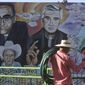 A gardener puts away his tools as he wraps up for the day backdropped by a mural featuring the late Archbishop Oscar Romero and Rev. Rutilio Grande in the Plaza de Los Martires or Martyrs Square, in El Paisnal, El Salvador, Friday, Jan. 21, 2022. Grande, a Jesuit priest who inspired St. Oscar Romero and was himself a victim of El Salvador’s right-wing death squads, will be beatified Saturday along with two Salvadorans who were killed with him. (AP Photo/Salvador Melendez)