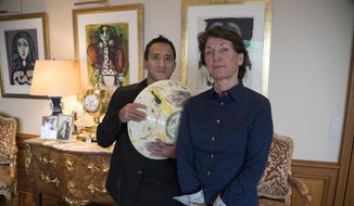 Marina Picasso, right, granddaughter of artist Pablo Picasso, and her son Florian Picasso pose with a ceramic art-work of Pablo Picasso in Cologny near in Geneva, Switzerland, Tuesday, Jan. 25, 2022. Heirs of Pablo Picasso, the famed 20th-century Spanish artist, are vaulting into 21st-century commerce by selling 1,010 digital art pieces of one of his ceramic works that has never before seen publicly — riding a fad for “crypto” assets that have taken the art and financial worlds by storm. (AP Photo/Boris Heger)