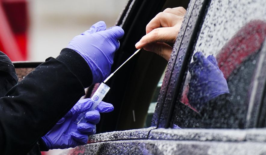 A driver places a swab into a vial at a free drive-thru COVID-19 testing site in the parking lot of the Mercy Fitzgerald Hospital in Darby, Pa., Thursday, Jan. 20, 2022. A requirement to get vaccinated against COVID-19 kicks in Thursday, Jan. 27,  for millions of health care workers in about half the states. (AP Photo/Matt Rourke, File)