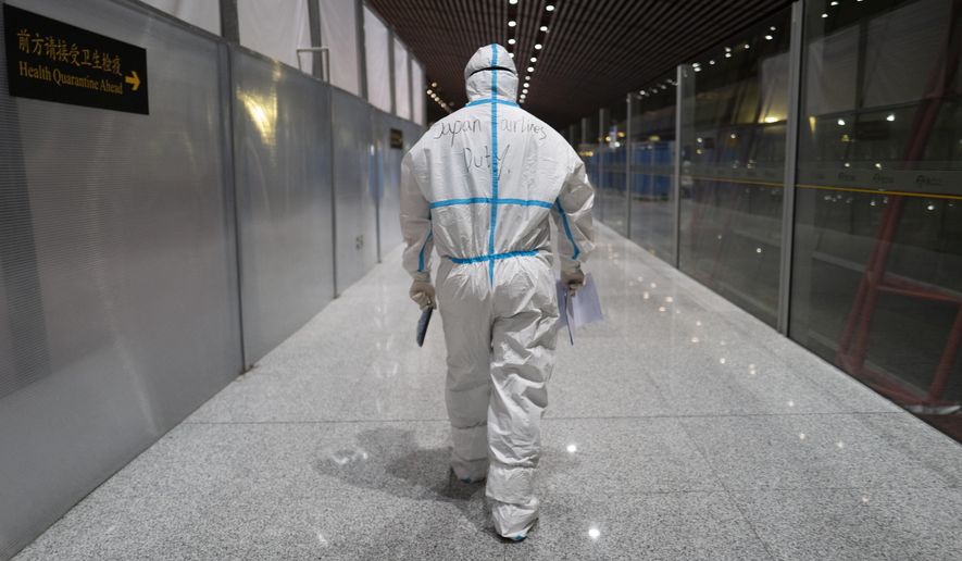 A member of airport personnel dressed in protective gear leads passengers into the customs area at the Beijing Capital International Airport ahead of the 2022 Winter Olympics in Beijing, Jan. 24, 2022. (AP Photo/Jae C. Hong, File)