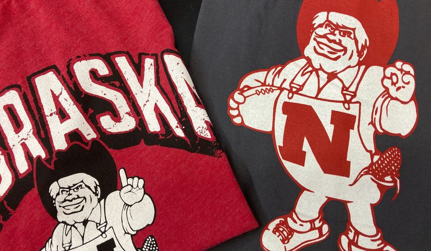 Nebraska Huskers t-shirts featuring new cartoon mascot Herbie Husker, left, and old cartoon mascot, right, are displayed at the Husker Hounds store in Omaha, Neb., Saturday, Jan. 29, 2022. The University of Nebraska-Lincoln has made a change to its cartoon mascot Herbie Husker to eliminate confusion about the meaning of a hand gesture he makes that some people connect with white supremacy.(AP Photo/Eric Olson)