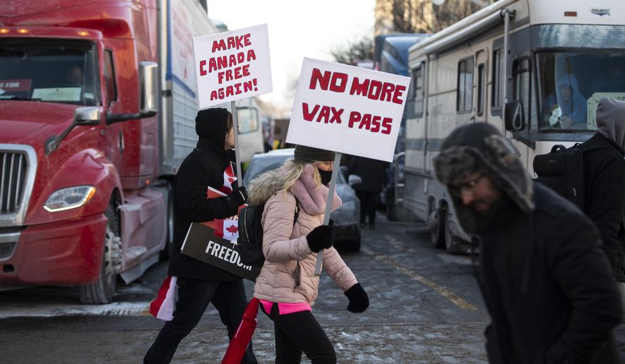 People walk in front of trucks parked on Wellington Street as they join a rally against COVID-19 restrictions on Parliament Hill, which began as a cross-country convoy protesting a federal vaccine mandate for truckers, in Ottawa, on Saturday, Jan. 29, 2022. (Justin Tang/The Canadian Press via AP)