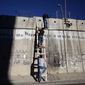 FILE - Palestinians use a ladder to climb over the separation barrier with Israel on their way to pray at the al-Aqsa Mosque in Jerusalem during the Muslim holy month of Ramadan, in Al-Ram, north of Jerusalem, July 11, 2014. Israel on Monday, Jan. 31, 2022, called on Amnesty International not to publish an upcoming report accusing it of apartheid, saying the conclusions of the London-based international human rights group are “false, biased and antisemitic.” (AP Photo/Majdi Mohammed, File)