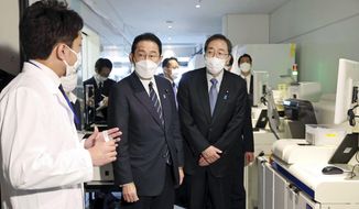 Japanese Prime Minister Fumio Kishida, center, listens to an official at an quarantine area at the Haneda international airport in Tokyo, Saturday, Feb. 12, 2022. Japan is considering easing its stringent border controls amid growing criticism that the measures, which have banned most foreign entrants including students and business travelers, are hurting the country&#39;s economy and international profile. (Japan Pool/Kyodo News via AP)