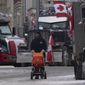 A protester walk past parked trucks with a baby carriage, Wednesday, Feb. 16, 2022, in Ottawa. (Adrian Wyld/The Canadian Press via AP)