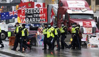 Ontario Provincial Police officers walk in front of the ongoing trucker blockade protest in Ottawa, Thursday, Feb. 17, 2022. Hundreds of truckers clogging the streets of Canada&#39;s capital city in a protest against COVID-19 restrictions are bracing for a possible police crackdown. (Adrian Wyld/The Canadian Press via AP)