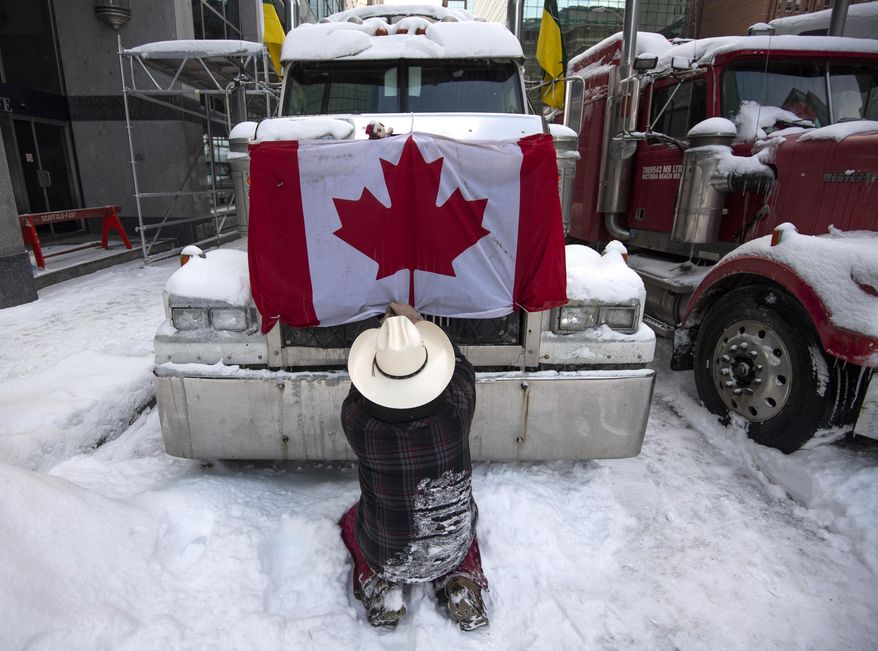 A trucker removes a flag of Canada from the hood of their vehicle as truckers prepare to drive away after participating in a blockade on Metcalfe Street as police begin clearing the streets near Parliament Hill to end to a protest which started in opposition to mandatory COVID-19 vaccine mandates and grew into a broader anti-government demonstration and occupation in Ottawa, Ontario, Saturday, Feb. 19, 2022. (Justin Tang/The Canadian Press via AP)