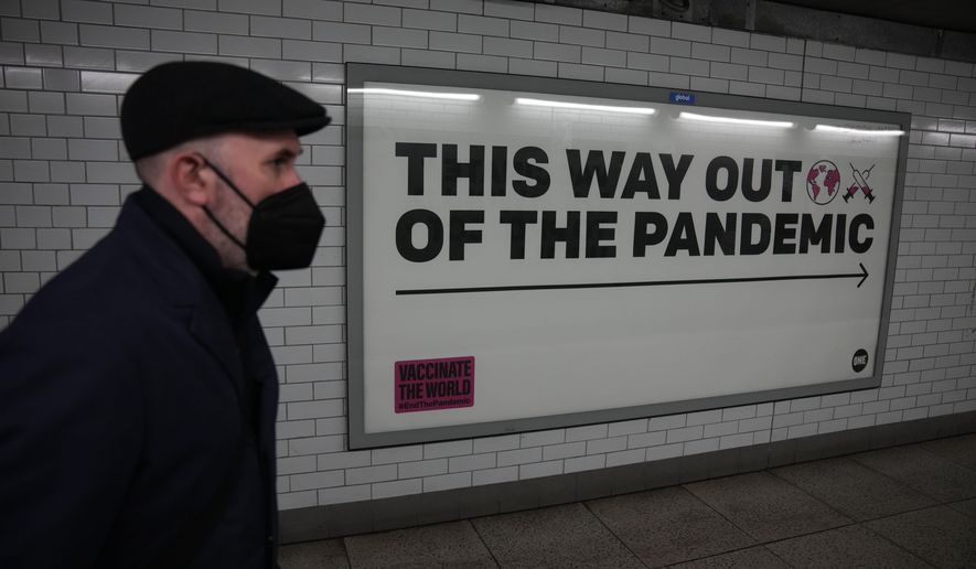 A man wearing a face mask to curb the spread of coronavirus walks past a health campaign poster from the One NGO, in an underpass leading to Westminster underground train station, in London, Thursday, Jan. 27, 2022. Scientists are warning the British government not to weaken the country’s ability to monitor and track the coronavirus when Prime Minister Boris Johnson ends the requirement for people in England to self-isolate if they contract COVID-19. Johnson will announce details in Parliament on Monday, Feb. 21, 2022 of the government’s plan for “living with COVID.” (AP Photo/Matt Dunham, File)