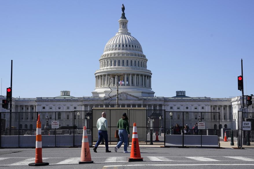 People walk past a security fence put in place in preparation for President Joe Biden's State of the Union address on Capitol Hill in Washington, Sunday, Feb. 27, 2022. (AP Photo/Patrick Semansky)