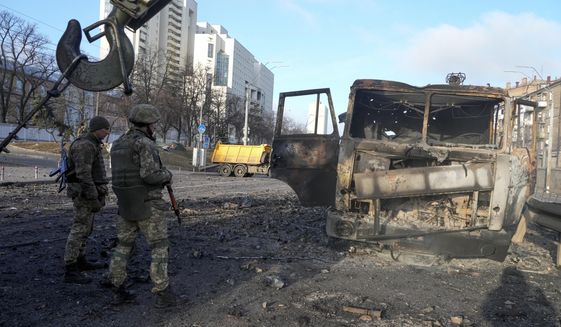 Ukrainian soldiers stand next to a burnt military truck, in a street in Kyiv, Ukraine, Saturday, Feb. 26, 2022. Russian troops stormed toward Ukraine&#39;s capital Saturday, and street fighting broke out as city officials urged residents to take shelter. (AP Photo/Efrem Lukatsky)
