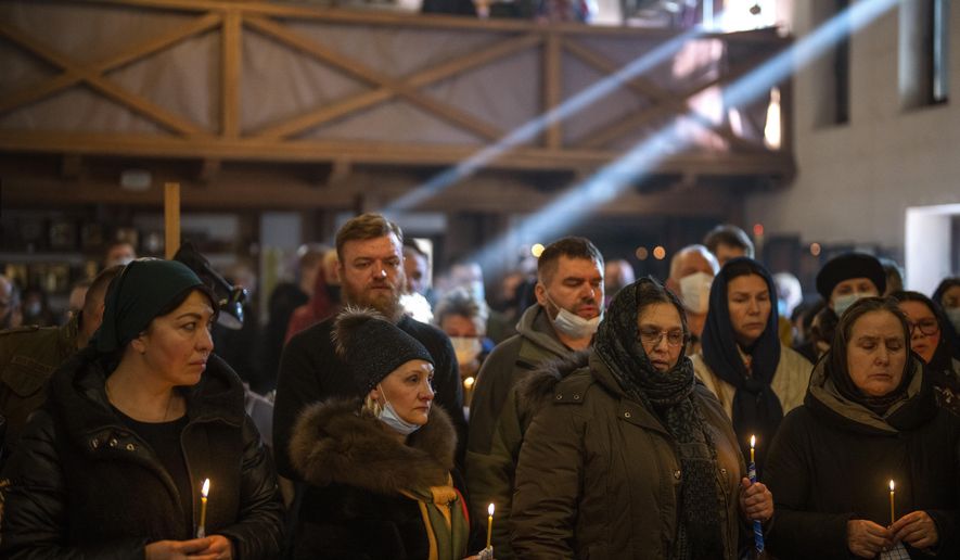 People pray next to the body of Ukrainian Army captain Anton Sydorov, 35, killed in eastern Ukraine, during his funeral in Kyiv, Ukraine, Tuesday, Feb. 22, 2022. (AP Photo/Emilio Morenatti, File)