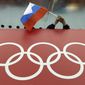 A Russian flag is held above the Olympic Rings at Adler Arena Skating Center during the Winter Olympics in Sochi, Russia on Feb. 18, 2014. The International Olympic Committee has made a sweeping move to isolate and condemn Russia over the country’s invasion of Ukraine. (AP Photo/David J. Phillip, File)