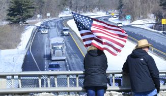Jessica, from Keene, N.H., holds an American flag at the I-91 Exit 2 overpass, in Brattleboro, Vt., to show support for the trucker convoy that passed through the area on Wednesday, March 2, 2022, as it makes its way down to Washington D.C. (Kristopher Radder/The Brattleboro Reformer via AP)