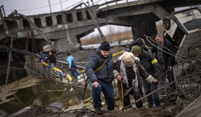 Local militiamen help an old woman crossing a bridge destroyed by artillery, as she tries to flee, on the outskirts of Kyiv, Ukraine, Wednesday, March 2. 2022. Russian forces have escalated their attacks on crowded cities in what Ukraine&#x27;s leader called a blatant campaign of terror. (AP Photo/Emilio Morenatti)