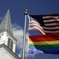 A gay pride rainbow flag flies along with the U.S. flag in front of the Asbury United Methodist Church in Prairie Village, Kan, on April 19, 2019. A group of theologically conservative United Methodists planned to launch a new worldwide denomination on May 1, 2022. This will begin the breakup of the third-largest religious body in the U.S.  (AP Photo/Charlie Riedel, File)