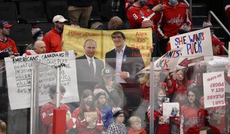 A sign is held up showing Vladimir Putin and Washington Capitals&#39; Alex Ovechkin during warmups before an NHL hockey game between the Capitals and the Seattle Kraken, Saturday, March 5, 2022, in Washington. (AP Photo/Nick Wass)