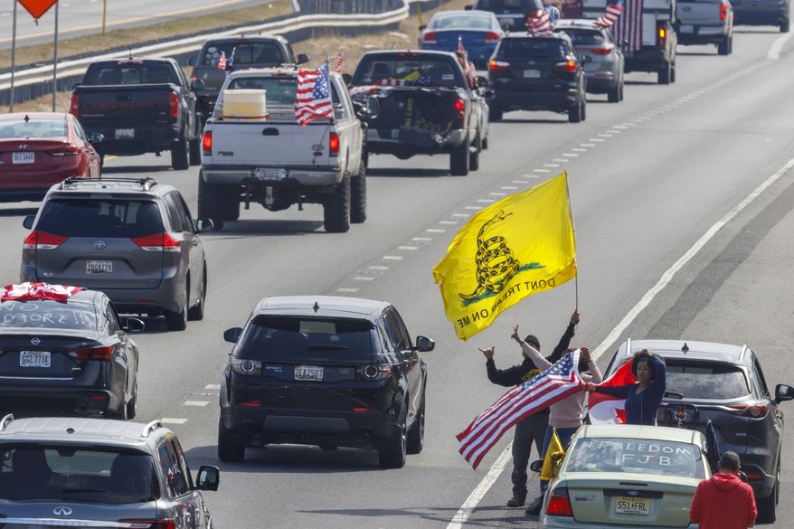 People on the side of the road watch as trucks and other vehicles with the People Convoy of Truckers, protesting COVID-19 mandates and other issues, head South on Interstate I-270 Sunday, March 6, 2022, in Frederick, Md., toward the Capital Beltway. (AP Photo/Jon Elswick)