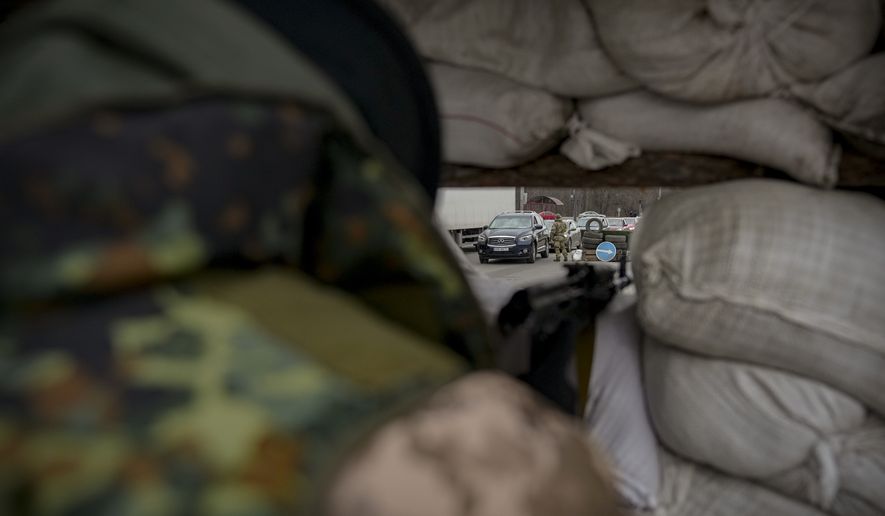 A Ukrainian serviceman monitors a checkpoint from behind sandbags on a main road in Kyiv, Ukraine, Monday, March 7, 2022. (AP Photo/Vadim Ghirda)