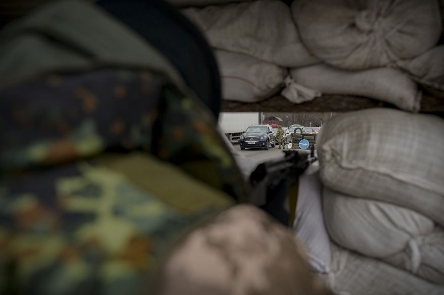 A Ukrainian serviceman monitors a checkpoint from behind sandbags on a main road in Kyiv, Ukraine, Monday, March 7, 2022. (AP Photo/Vadim Ghirda)