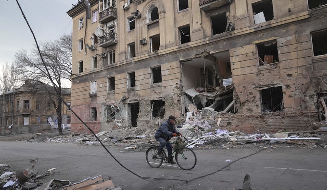 A man rides a bicycle in front of a damaged by shelling apartment building in Mariupol, Ukraine, Wednesday, March 9, 2022. (AP Photo/Evgeniy Maloletka)