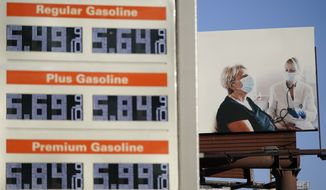 A billboard showing a woman getting her blood pressure taken stands behind a sign displaying gas prices in downtown Los Angeles, Wednesday, March 9, 2022. The average price for a gallon of gasoline in the U.S. hit a record $4.17 on Tuesday as the country prepares to ban Russian oil imports. (AP Photo/Ashley Landis)