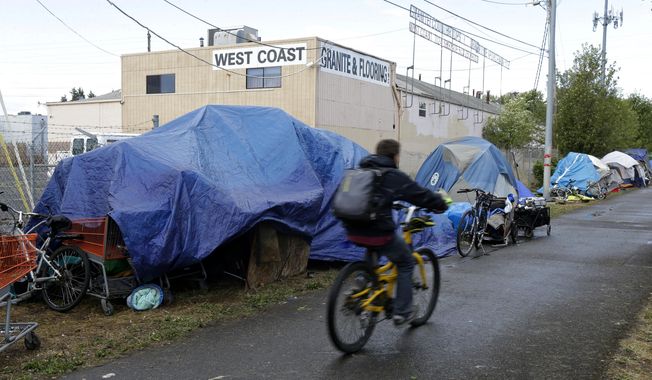 A person cycles past tents used by people experiencing homelessness set up along a pathway in Portland, Ore., on Sept. 19, 2017. For years, liberal cities in the U.S have tolerated people living in tents in parks and public spaces, but increasingly leaders in places like Portland, Oregon, New York and Seattle are removing encampments and pushing other strict measures that would&#x27;ve been unheard of a few years ago. (AP Photo/Ted S. Warren, File)