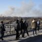 Pedestrians walk over an overpass as a cloud of smoke raises after an explosion in Lviv, Western Ukraine, Friday, March 18, 2022. The mayor of Lviv says missiles struck near the city&#39;s airport early Friday. (AP Photo/Bernat Armangue)