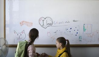 Two refugee children from the Ukraine stand in front of a white board before their classes start in Berlin, Germany, Monday, March 21, 2022. Forty Ukrainian refugee children started their first day of elementary school in Berlin on Monday only weeks after they fled the war back home. The two private refugee classes were put together by two Berlin volunteers who managed to raise funds, get free class rooms. (AP Photo/Markus Schreiber)