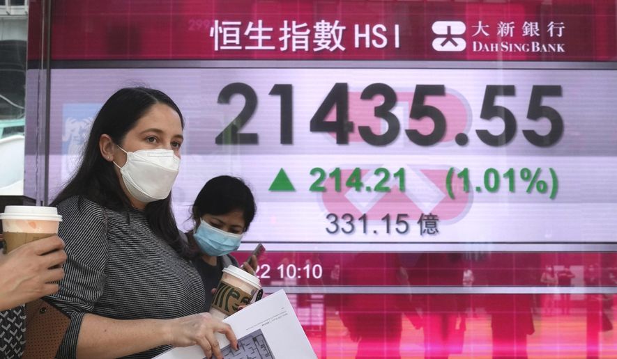 A woman wearing a face mask walks past a bank's electronic board showing the Hong Kong share index in Hong Kong, Tuesday, March 22, 2022. Asian shares were mostly higher Tuesday as investors eyed the war in Ukraine, inflationary risks and surging energy prices. (AP Photo/Kin Cheung)