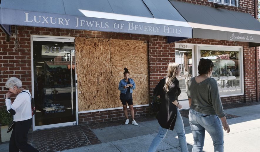 Pedestrians walk past a boarded up Luxury Jewels of Beverly Hills on Wednesday, March 23, 2022 in Beverly Hills, Calif. Los Angeles police are warning people that wearing expensive jewelry in public could make them a target for thieves a note of caution as robberies are up citywide. The police department's suggestion Tuesday came as robbers smashed the front window of the Beverly Hills jewelry store in broad daylight and fled with millions of dollars' worth of merchandise. (AP Photo/Richard Vogel)