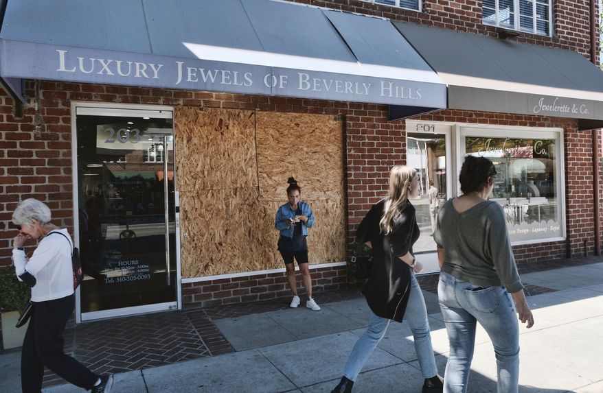Pedestrians walk past a boarded up Luxury Jewels of Beverly Hills on Wednesday, March 23, 2022 in Beverly Hills, Calif. Los Angeles police are warning people that wearing expensive jewelry in public could make them a target for thieves a note of caution as robberies are up citywide. The police department's suggestion Tuesday came as robbers smashed the front window of the Beverly Hills jewelry store in broad daylight and fled with millions of dollars' worth of merchandise. (AP Photo/Richard Vogel)