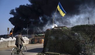 A man rides a bicycle as black smoke rises from a fuel storage of the Ukrainian army following a Russian attack, on the outskirts of Kyiv, Ukraine, Friday, March 25, 2022. (AP Photo/ (AP Photo/Rodrigo Abd)