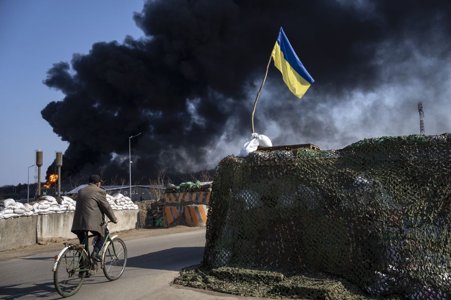 A man rides a bicycle as black smoke rises from a fuel storage of the Ukrainian army following a Russian attack, on the outskirts of Kyiv, Ukraine, Friday, March 25, 2022. (AP Photo/ (AP Photo/Rodrigo Abd)