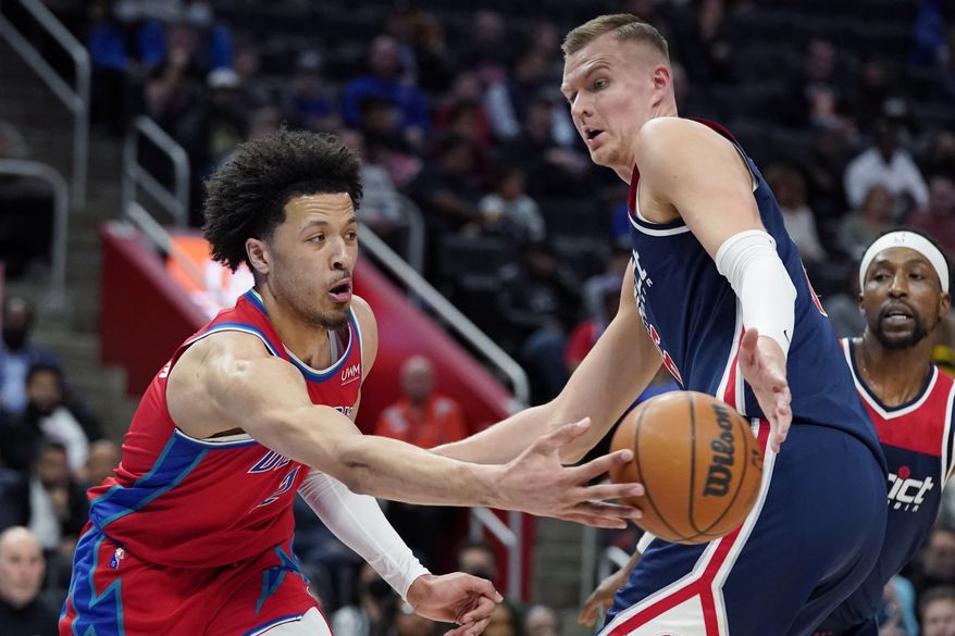 Detroit Pistons guard Cade Cunningham passes around Washington Wizards center Kristaps Porzingis during the first half of an NBA basketball game, Friday, March 25, 2022, in Detroit. (AP Photo/Carlos Osorio)