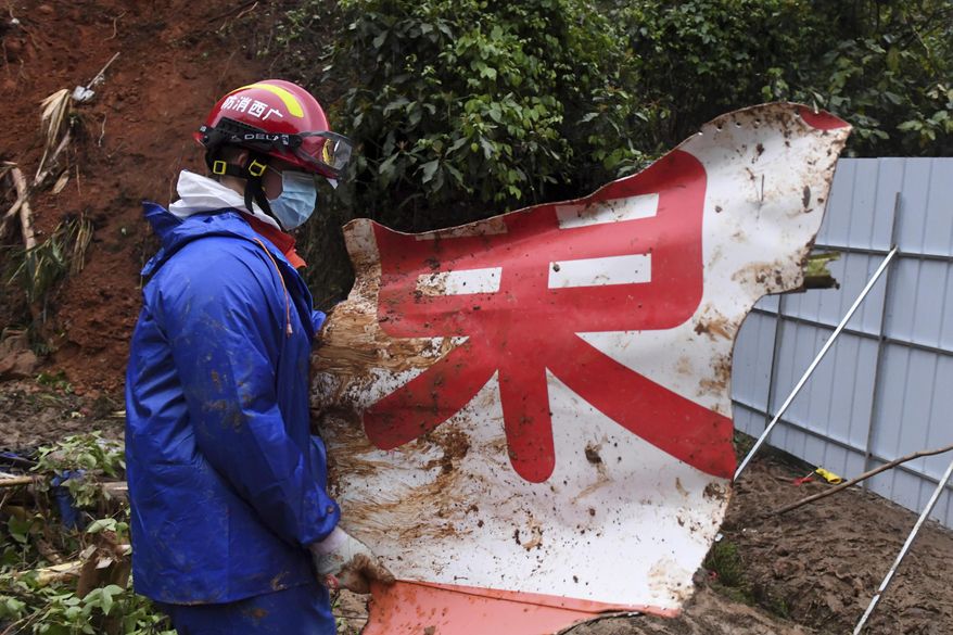 In this photo released by Xinhua News Agency, a rescue team member carries a piece of debris at the China Eastern flight crash site in Tengxian County in southern China's Guangxi Zhuang Autonomous Region on Thursday, March 24, 2022. Hundreds of people in rain gear and rubber boots searched muddy, forested hills in southern China on Thursday for the second flight recorder from a jetliner that crashed with 132 people aboard. (Lu Boan/Xinhua via AP)