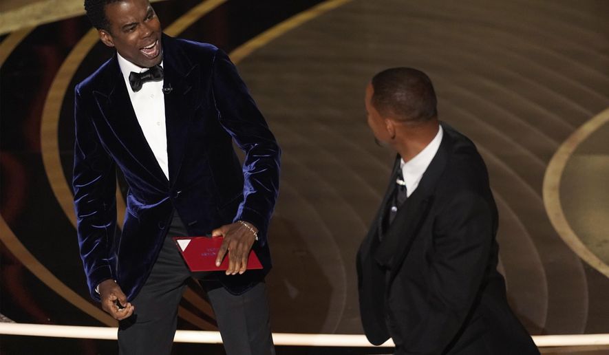 presenter Chris Rock, left, reacts after being hit on stage by Will Smith while presenting the award for best documentary feature at the Oscars on Sunday, March 27, 2022, at the Dolby Theatre in Los Angeles. (AP Photo/Chris Pizzello)