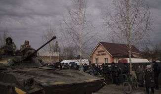 Residents lining up for aid watch as Ukrainian soldiers ride atop a tank in the town of Trostsyanets, Ukraine, Monday, March 28, 2022. Trostsyanets was recently retaken by Ukrainian forces after being held by Russians since the early days of the war. (AP Photo/Felipe Dana)