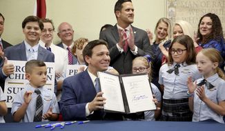 Florida Gov. Ron DeSantis displays the signed Parental Rights in Education, aka the Don&#39;t Say Gay bill, flanked by elementary school students during a news conference on Monday, March 28, 2022, at Classical Preparatory school in Shady Hills. (Douglas R. Clifford/Tampa Bay Times via AP)
