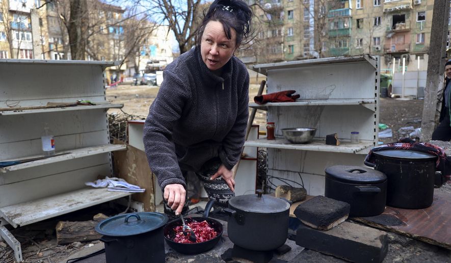 A woman cooks in a yard of apartment buildings damaged by shelling from fighting on the outskirts of Mariupol, Ukraine, in territory under control of the separatist government of the Donetsk People's Republic, on Tuesday, March 29, 2022. (AP Photo/Alexei Alexandrov)