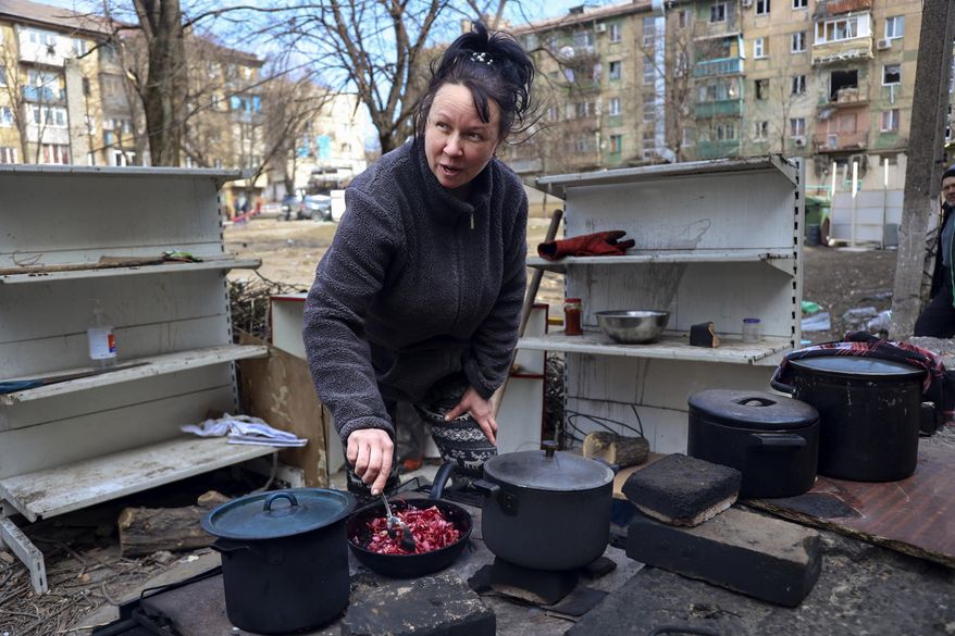 A woman cooks in a yard of apartment buildings damaged by shelling from fighting on the outskirts of Mariupol, Ukraine, in territory under control of the separatist government of the Donetsk People's Republic, on Tuesday, March 29, 2022. (AP Photo/Alexei Alexandrov)