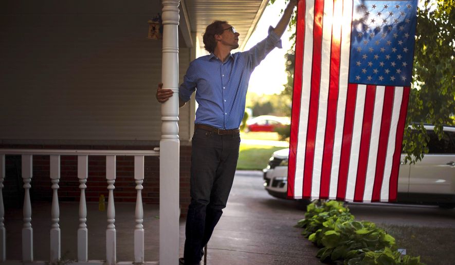 In this Aug. 18, 2020, file photo, Outagamie County Executive Tom Nelson adjusts the American flag hanging off his front porch in Appleton, Wis. (AP Photo/David Goldman, File)