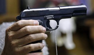 A sales clerk holds a pistol during an auction in Rochester, Wash., on Oct. 20, 2017. (AP Photo/Elaine Thompson, File)