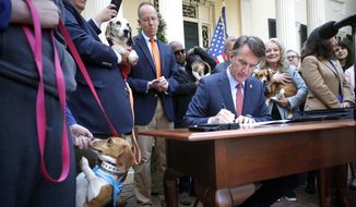 Emily Neal feeds her adopted dog Tannis a treat as Gov. Glenn Youngkin signs five bills to penalize animal cruelty and prohibit the sale of dogs or cats for experimental purposes on Monday, April 4, 2022 in Richmond, Va.    (Alexa Welch Edlund/Richmond Times-Dispatch via AP)
