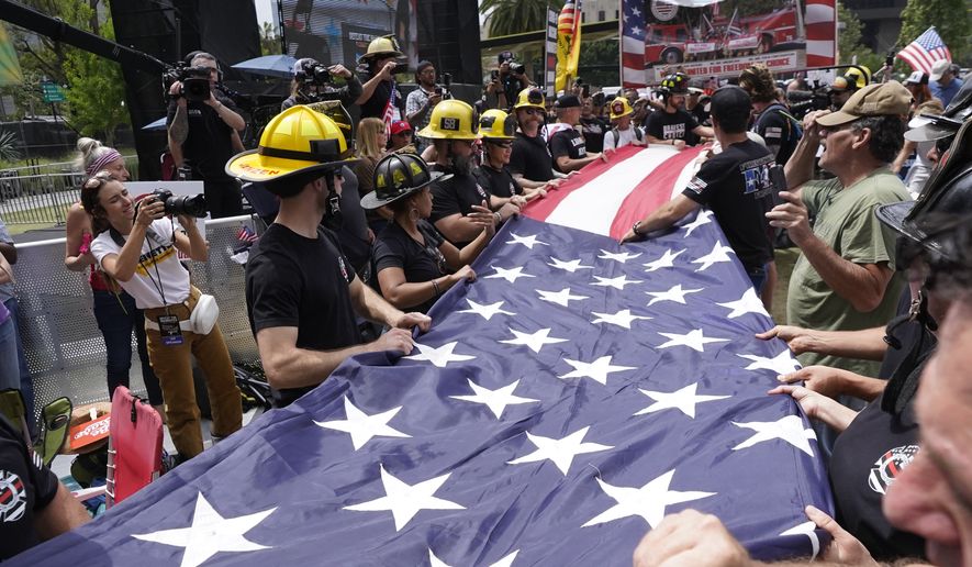 Firefighters with Bravest for Choice prepare to fold a large U.S. flag as they protest vaccination mandates designed to slow the spread of COVID-19 in Los Angeles Sunday, April 10, 2022. The crowd rallied at Grand Park to hear speakers and performers while big-rig trucks from the &quot;People&#39;s Convoy&quot; were parked on nearby streets. Los Angeles County and the city require their workers, including firefighters and police and sheriff&#39;s deputies, to be fully vaccinated or to have medical or religious exemptions. Relatively few have faced disciplinary action. The city has successfully fought anti-mandate lawsuits filed on behalf of firefighters and police department workers. (AP Photo/Damian Dovarganes)