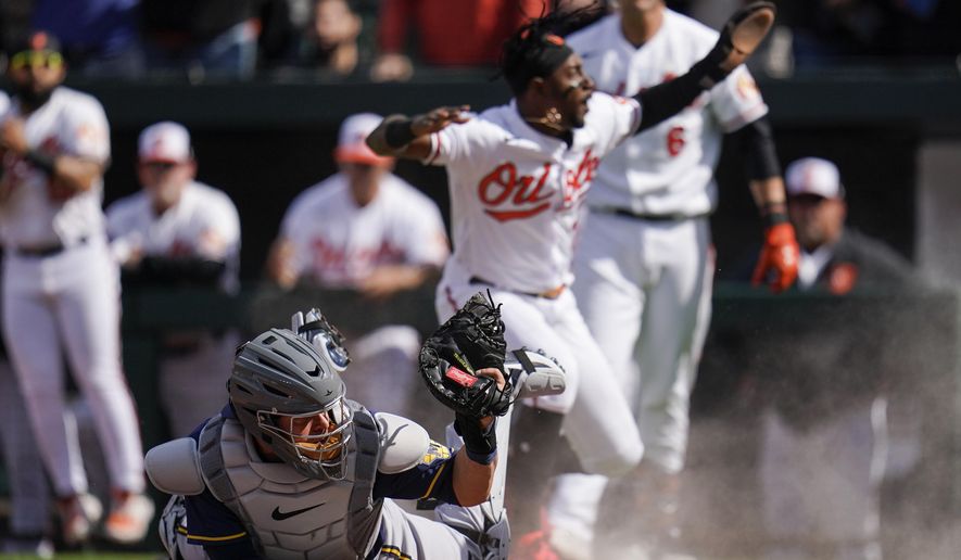 Milwaukee Brewers catcher Victor Caratini, left, holds up the ball after missing the tag on Baltimore Orioles&#x27; Jorge Mateo, back, who scores on a single by Jorge Mateo during the second inning of a baseball game at Oriole Park at Camden Yards, Monday, April 11, 2022, in Baltimore. (AP Photo/Julio Cortez)