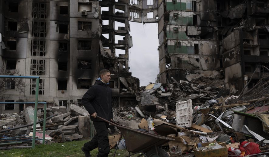 A young man pushes a wheelbarrow in front of a destroyed apartment building in the town of Borodyanka, Ukraine, on Sunday, April 10, 2022. (AP Photo/Petros Giannakouris)