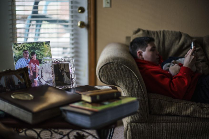 Landon Quackenbush, 13, right, lies on the couch next to a photo of him and his father, Larry Quackenbush, at their home in Springfield, Mo., Tuesday, March 22, 2022. Larry, 60, was the glue that held his family together. He got sick with COVID-19 after Landon arrived home from summer camp in July. First Larry, then his wife were rushed to the hospital. She was able to return home a day later, but her husband remained, tethered to a ventilator. He died on Aug. 3. (AP Photo/David Goldman)